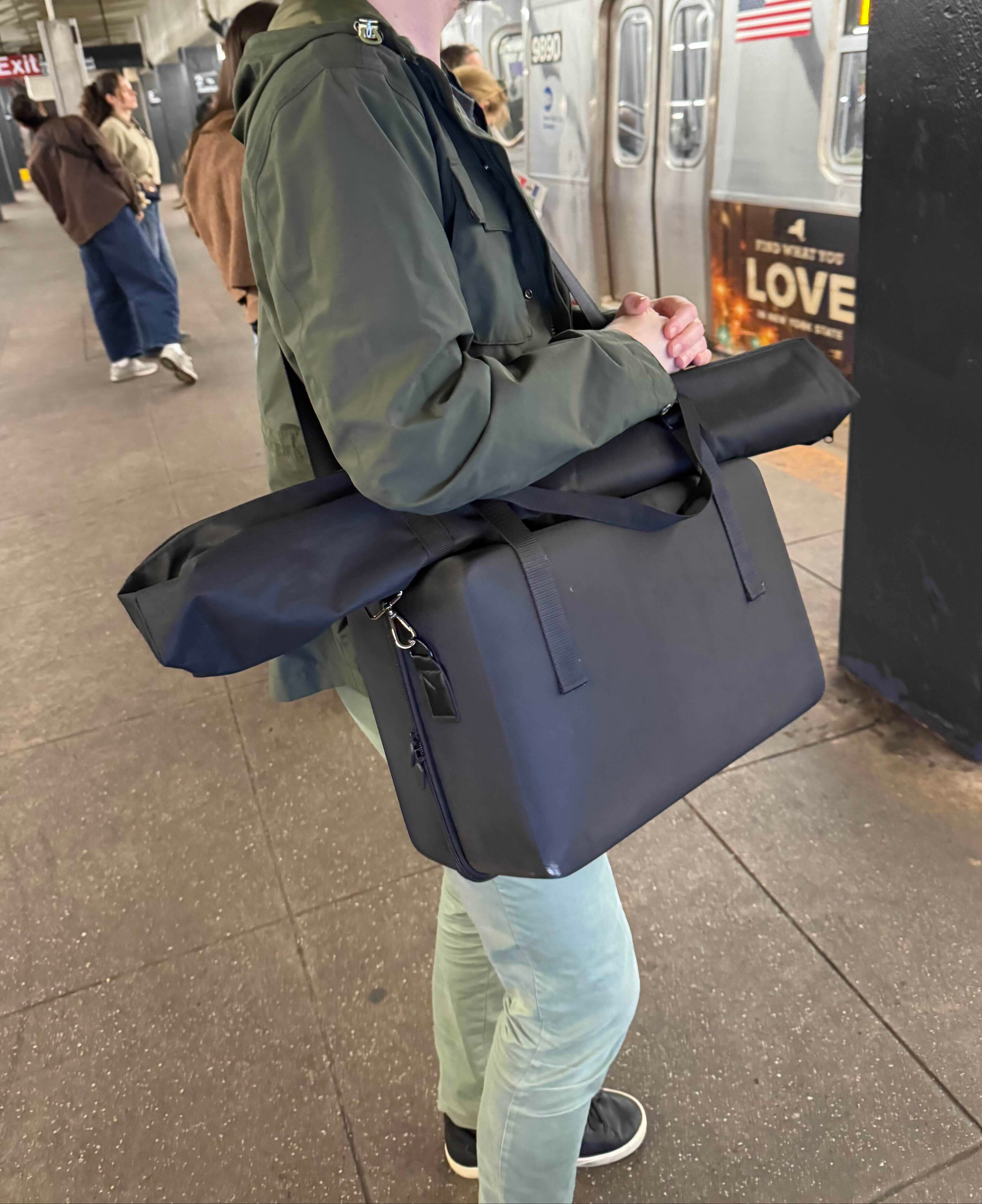 Person carrying portable mannequin in black carry case waiting for subway.